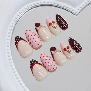 Pink French almond press-on nails with red cherry patterns and 3D bow accents