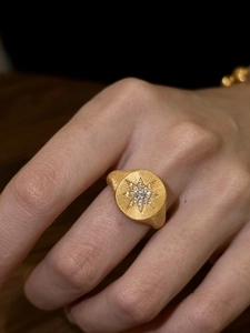Macro shot of a gold starburst signet ring with small stones on a model finger