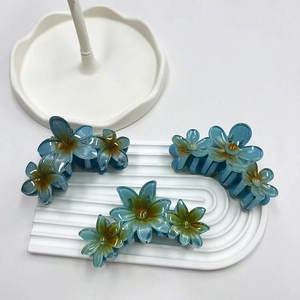 Dettaglio di tre mollette per capelli a forma di plumeria blu su un vassoio bianco