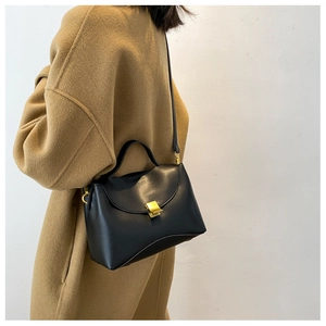 Close-up of a black leather handbag with gold buckle held by a model in a beige coat
