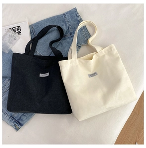 Detailed close-up of black and cream corduroy tote bags with fashion label on white bedding