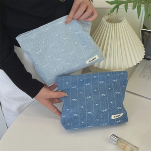 Detail of denim cosmetic bag with white bow embroidery and a side brand label