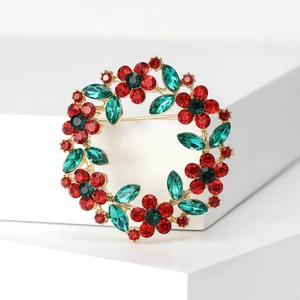 Elegant gold floral wreath brooch with red crystals and green rhinestone leaves on white stand