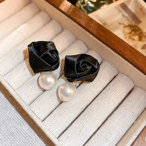 Macro detail of black fabric rose earrings with pearl drop on a jewelry display box
