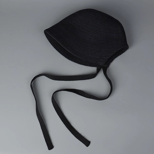 Detailed flat lay of a black handmade knit bonnet hat with tie strings on grey background