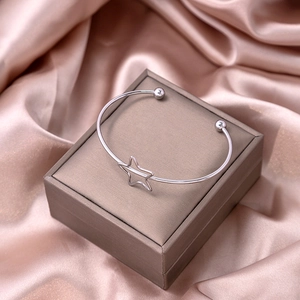 Close-up of a silver star-shaped open bangle on a champagne silk display box