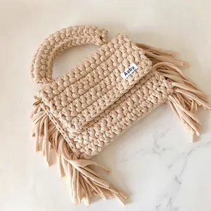 Close-up of handmade crochet bag featuring fabric tassels and a brand woven label