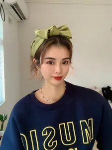 Detail shot of a large grass green satin bow headband worn by a model in a casual setting
