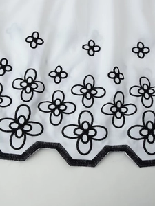 Close-up of white fabric with black floral embroidery and wavy scalloped edge hem