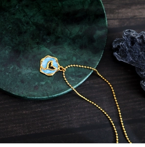 Macro detail of golden whale tail pendant with blue enamel on a green marble stand