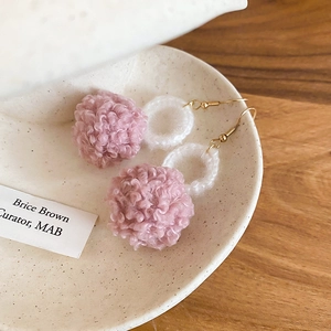 Dettaglio degli orecchini con pompon rosa e cerchio intrecciato bianco su ceramica