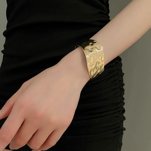Close-up of golden hammered wide cuff bracelet with irregular textured metal surface