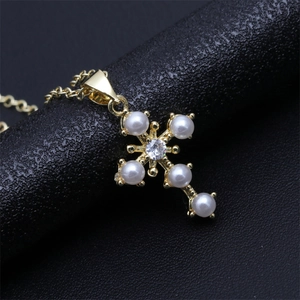 Detail of gold cross pendant necklace featuring white pearls and zircon on black background