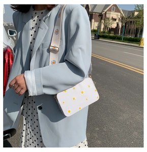 Street style shot of a white crossbody bag with floral daisy embroidery and a wide strap