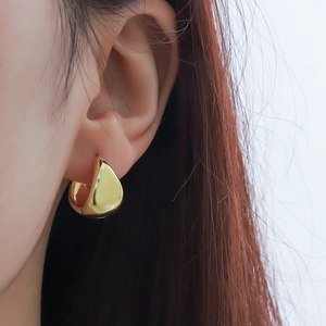 Close-up of polished gold teardrop hoop earrings on model for a minimalist style