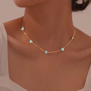 Detailed view of a gold collar necklace with five blue and white heart charms on a model