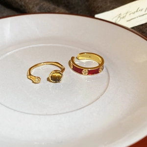 Detailed macro view of 18k gold plated tiger eye ring and red enamel coin band on a tray