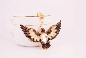 Detail of an eagle keychain with crystal chest and enamel wings on a white ceramic cup