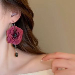 Detailed view of deep red fabric rose earrings with black teardrop beads on silver loops
