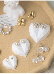 Macro shot of gold floral earrings and pearl bracelets on heart shaped display stands