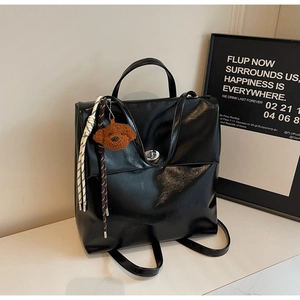Detail of black leather backpack featuring a vintage twist lock and brown teddy bear charm