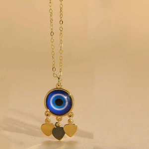 Detail shot of golden evil eye necklace featuring blue zircon and three heart charms