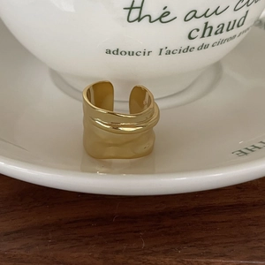 Detail of minimalist gold-plated wavy ring on a cream saucer with a French-style aesthetic