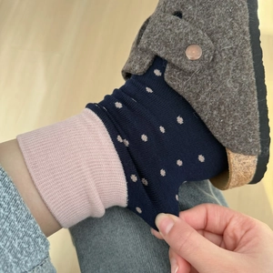 Close-up of navy blue polka dot socks with pink ribbed cuffs and felt clogs on wood floor