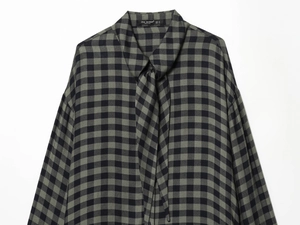 Detail of grey-green plaid shirt collar featuring a pussy-bow tie and garment brand label