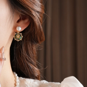 Close-up of gold starburst earrings with green enamel and pearls on model
