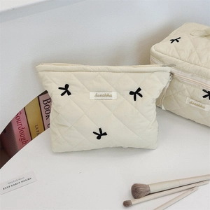 Detail of embroidered bow patterns on cream quilted cotton cosmetic bags and organizer