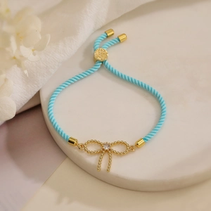 Blue woven bracelet with gold bow pendant and zircon center on marble background