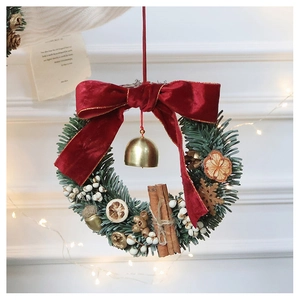 Detail of Christmas wreath with red velvet bow, pine needles, cinnamon, and golden bells