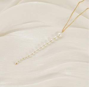 Gros plan d'un collier de perles dorées sur soie blanche, design minimaliste et long