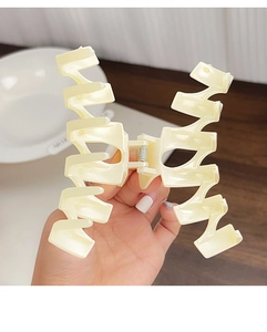 Détail d'une grande pince à cheveux ondulée crème tenue à la main avec ressort en métal