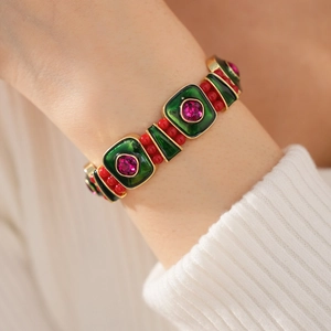 Detail of vintage style bracelet with green enamel, red beads, and gold-plated frames