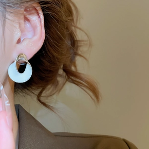 Detailaufnahme eines silbernen Ohrrings mit weißer Emaille am Ohr eines Models