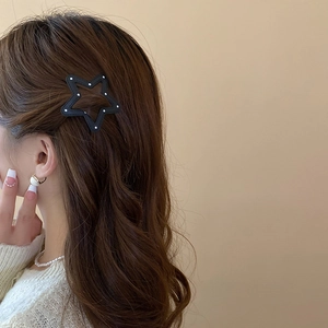 Star-shaped black hair clip with white polka dots worn on a woman's brown wavy hair
