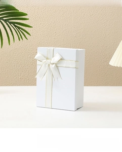 Detail view of large white foldable gift box with gold-edged cream ribbon and bow