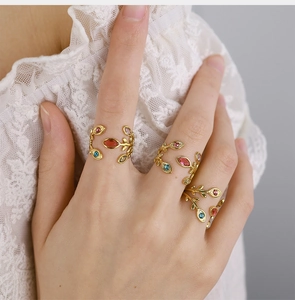 Three 18K gold leaf rings with colorful zircon crystals worn on a hand over white lace