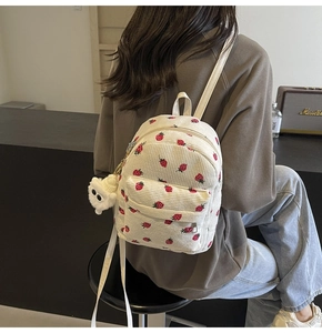 Detail of beige corduroy backpack with red strawberry pattern and plush charm pendant