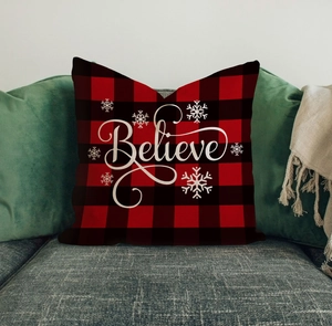 Detail of red and black buffalo plaid Christmas pillow with white Believe text on gray sofa
