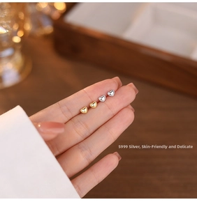 Macro shot of S999 sterling silver heart studs in gold and silver finish between fingers