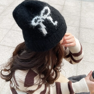 Detailed close-up of a black knit beanie featuring a large plush white bow pattern