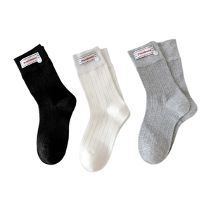 Three pairs of ribbed mid-calf socks in black, white, and grey with branded labels