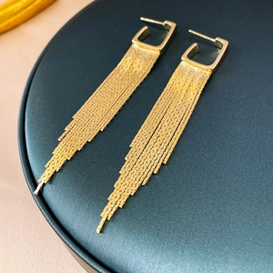 Close-up of golden geometric tassel earrings with cascading chains on a black jewelry stand