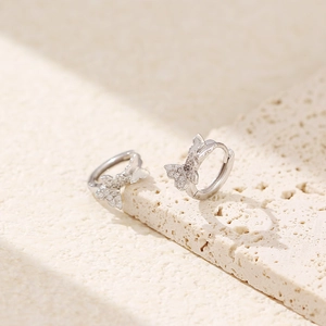 Detailed view of S925 silver butterfly earrings with zircons on beige stone surface