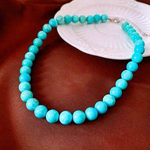 Vue détaillée du collier en perles de turquoise avec fermoir argenté sur fond en soie