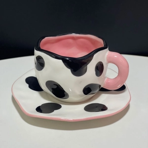 Detail of irregular ceramic coffee cup with cow print patterns and pink handle