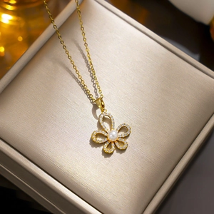 Elegant gold butterfly necklace with inlaid gems and central pearl in a beige jewelry box